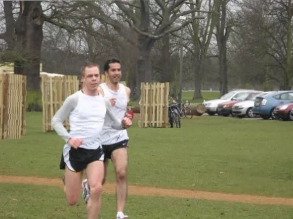 A parkrunner crosses a finish line in a wooded park setting