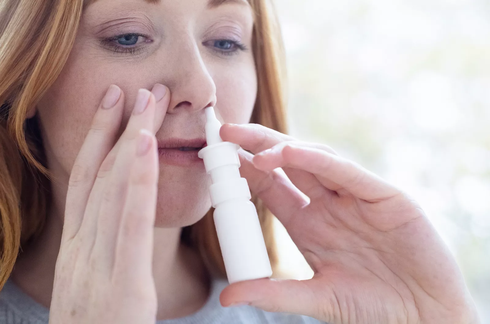 A woman holding a nasal spray bottle in a living room