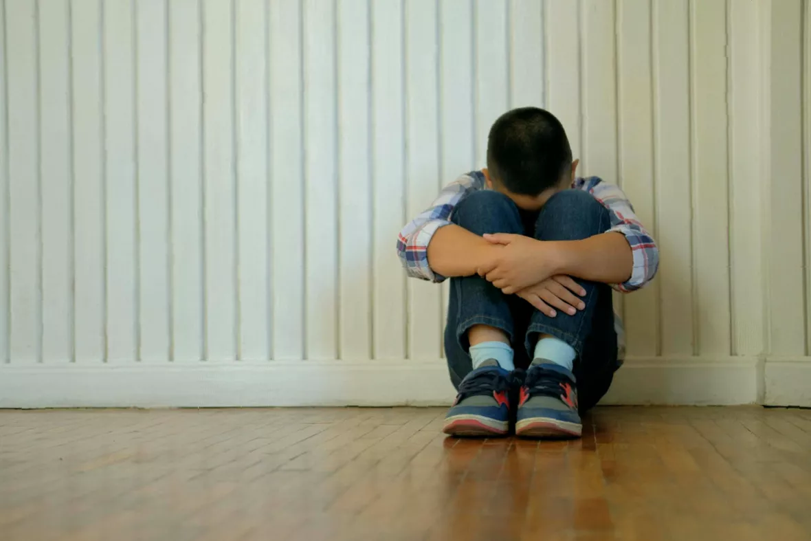 A child sitting alone on a school bench looking upset