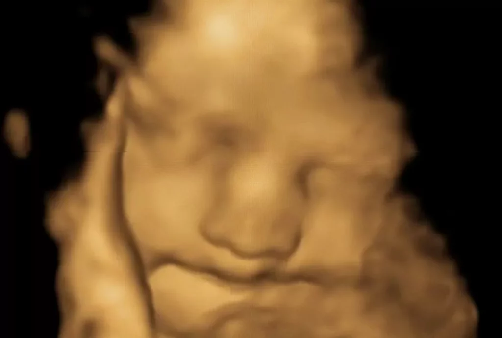A pregnant woman holding a glass of vegetable juice in a kitchen setting