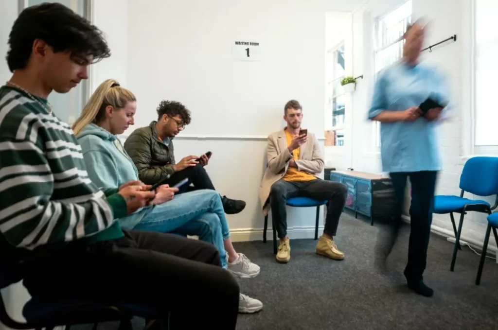 GP practice waiting room in England with patients seated