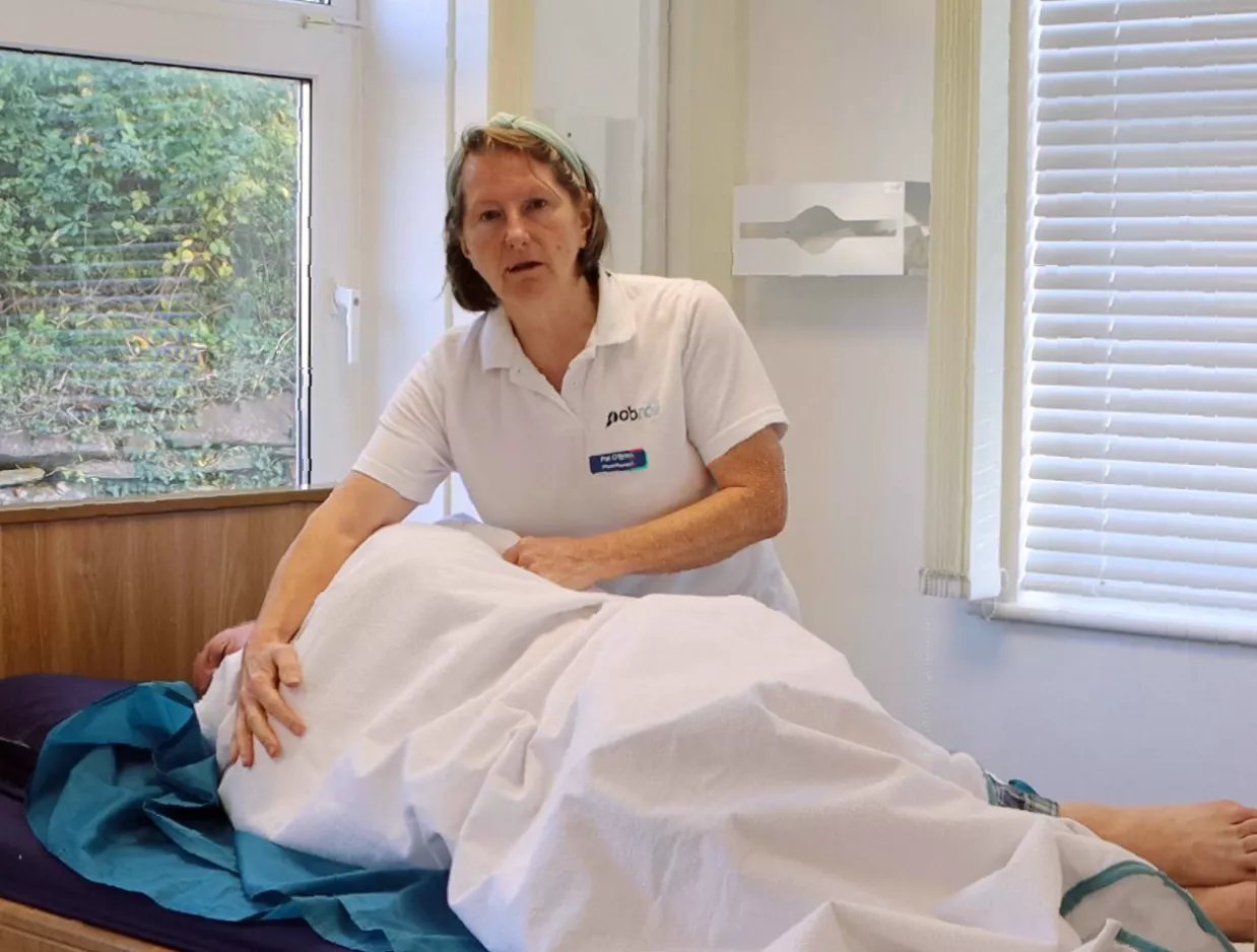 Carers using a protective towel roll to wash a patient discreetly in bed