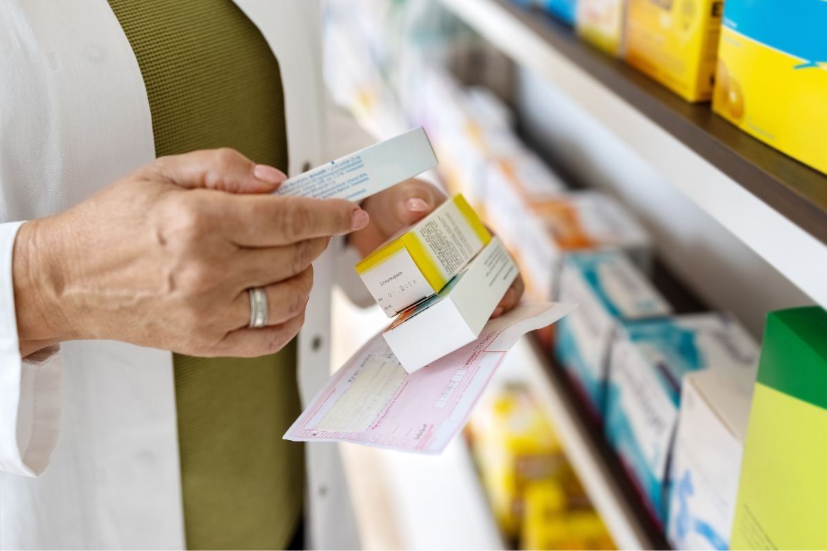 Patient leaflets and prescription medicines arranged on a shelf behind a pharmacy consultation room desk.