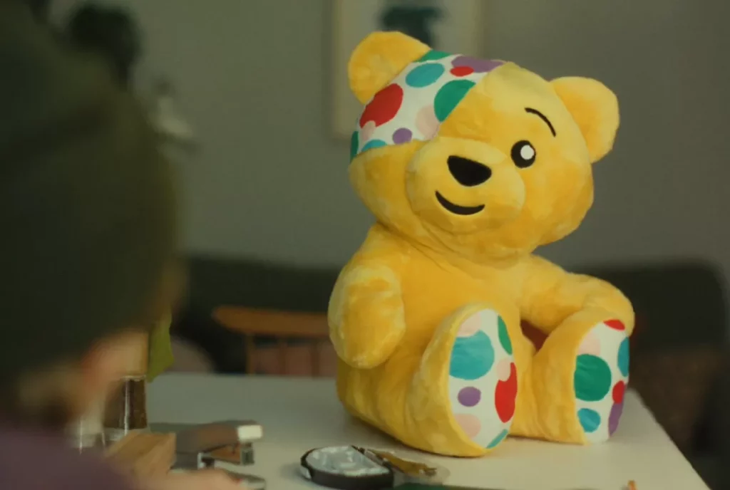 A yellow mascot bear talks with a young boy in a televised mental health awareness advert