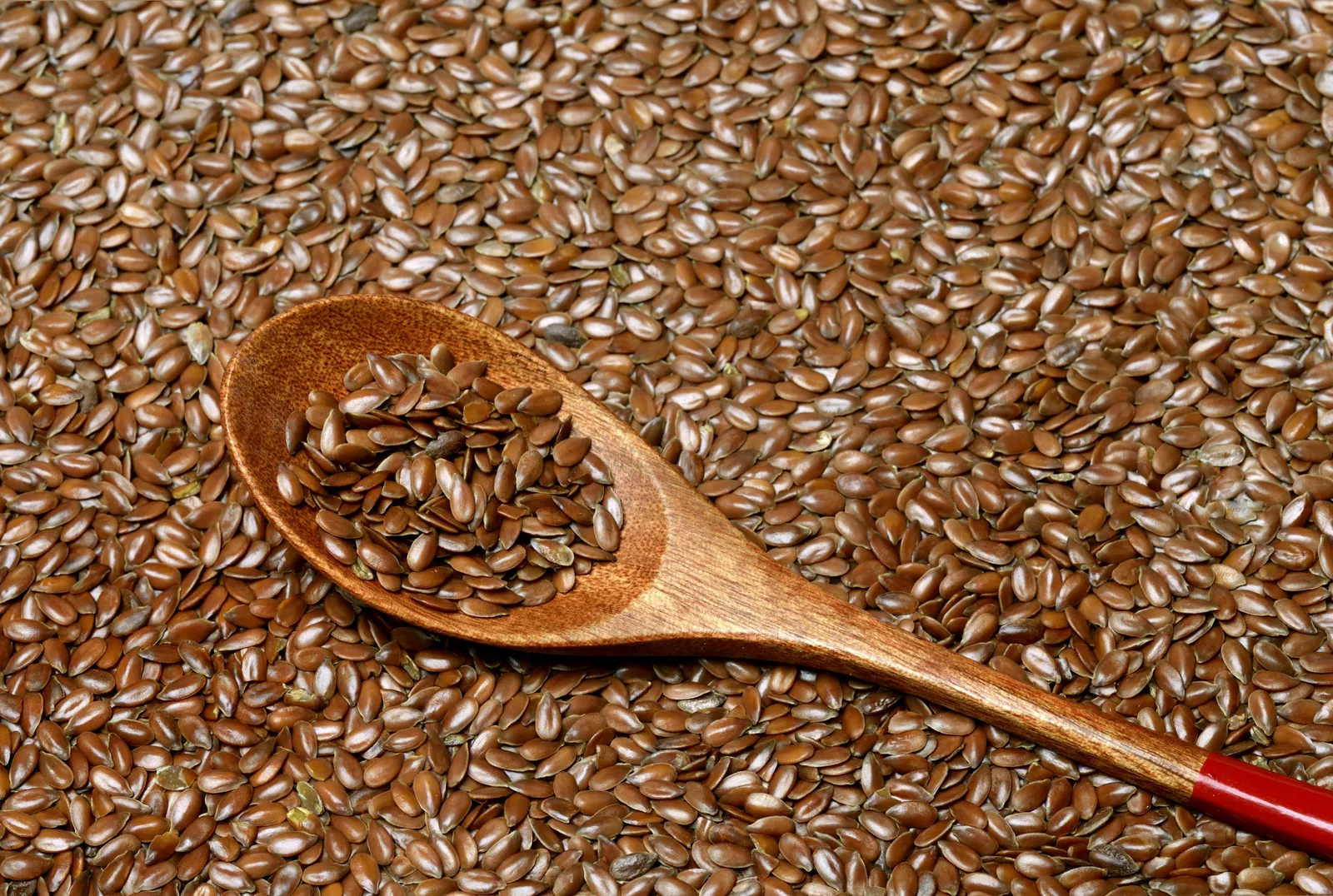 A close-up of ground flaxseed in a wooden spoon on a table