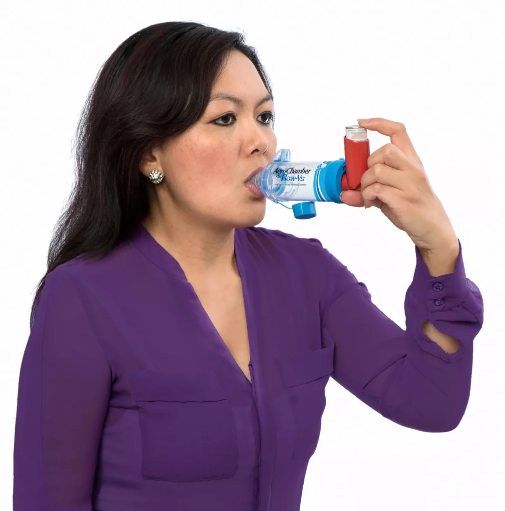 A person holding a pressurised metered-dose inhaler with a spacer device attached