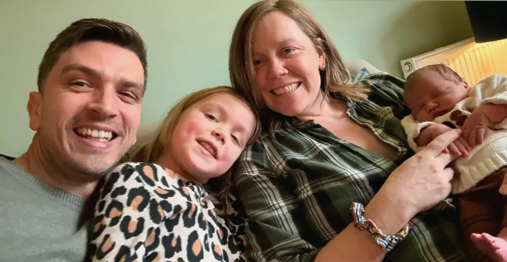 Woman sitting on sofa holding positive pregnancy test after years of fertility treatment