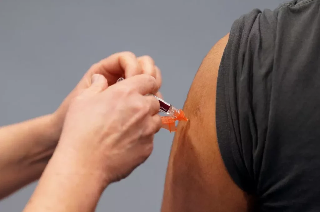A young person receiving a meningitis B vaccination injection from a pharmacist in a consultation room.