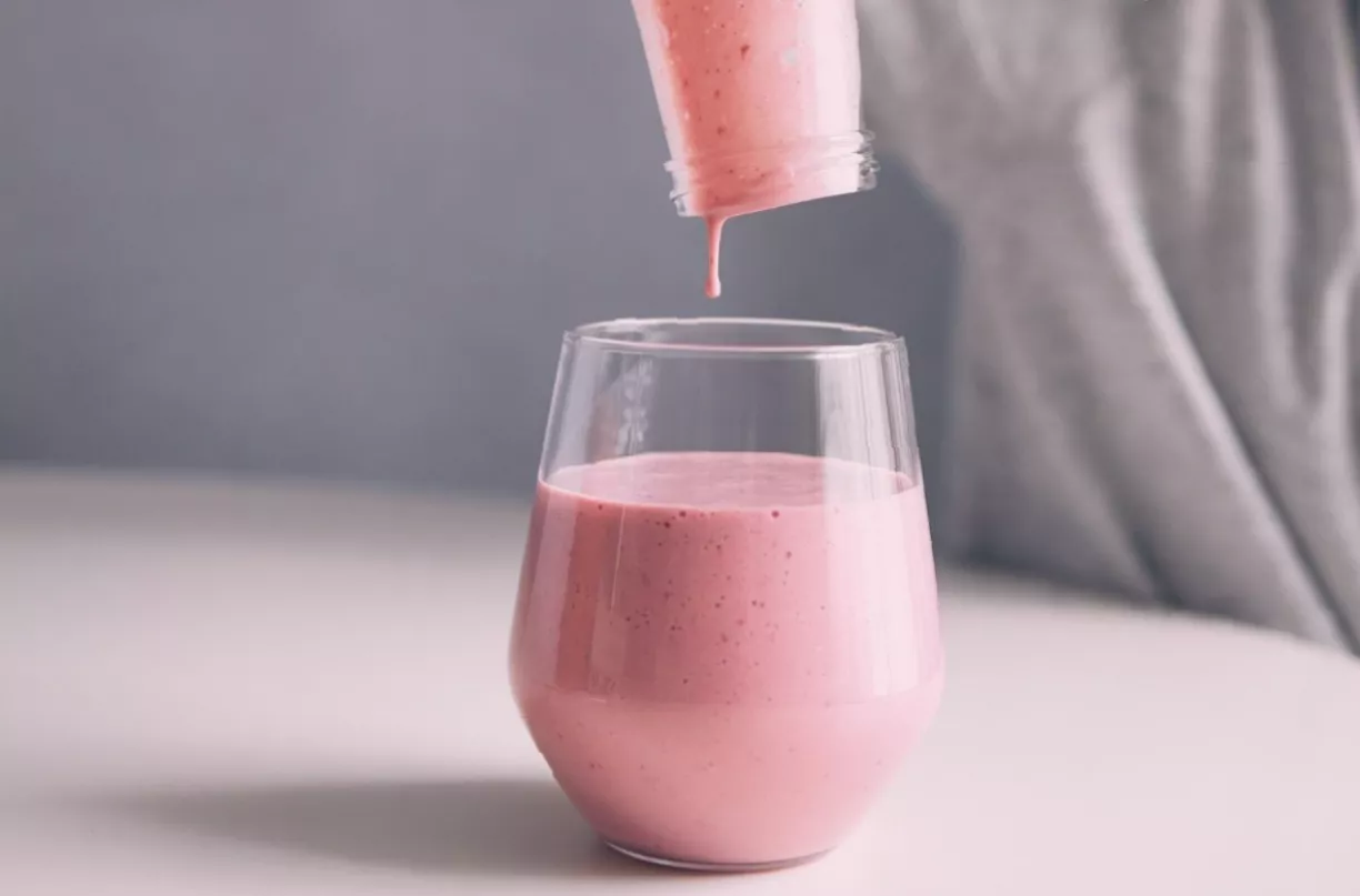 A measuring spoon of plant sterol granules beside a glass of milk