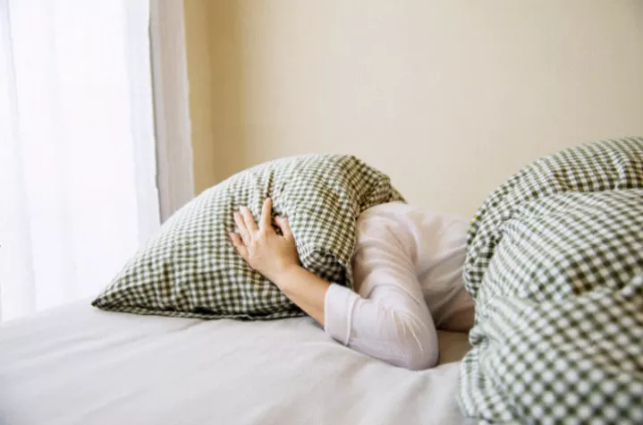A person lying awake in bed at night, illuminated by a phone screen