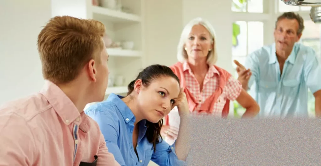 Midlife parents at a kitchen table looking worried, with adult child's bedroom door closed in background
