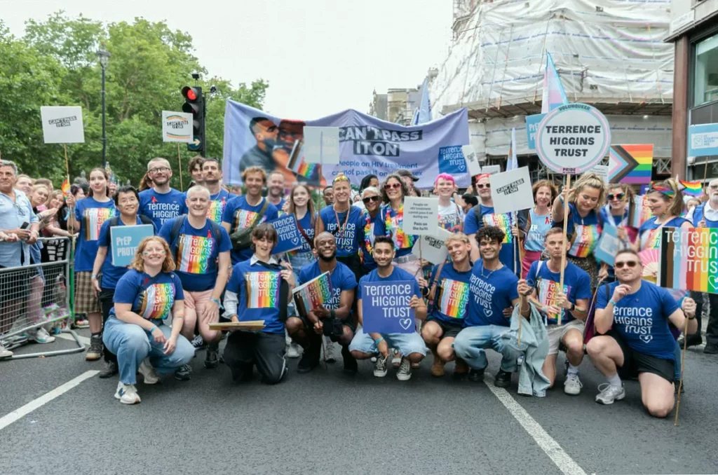 A charity helpline office worker speaking on a phone at a desk with a rainbow flag visible in the background.